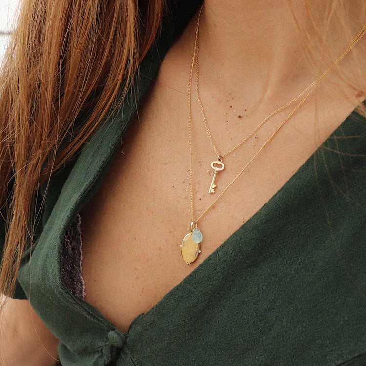 Image is a delicate brass key pendant with a gold filled chain handmade by Izaskun Zabala.
